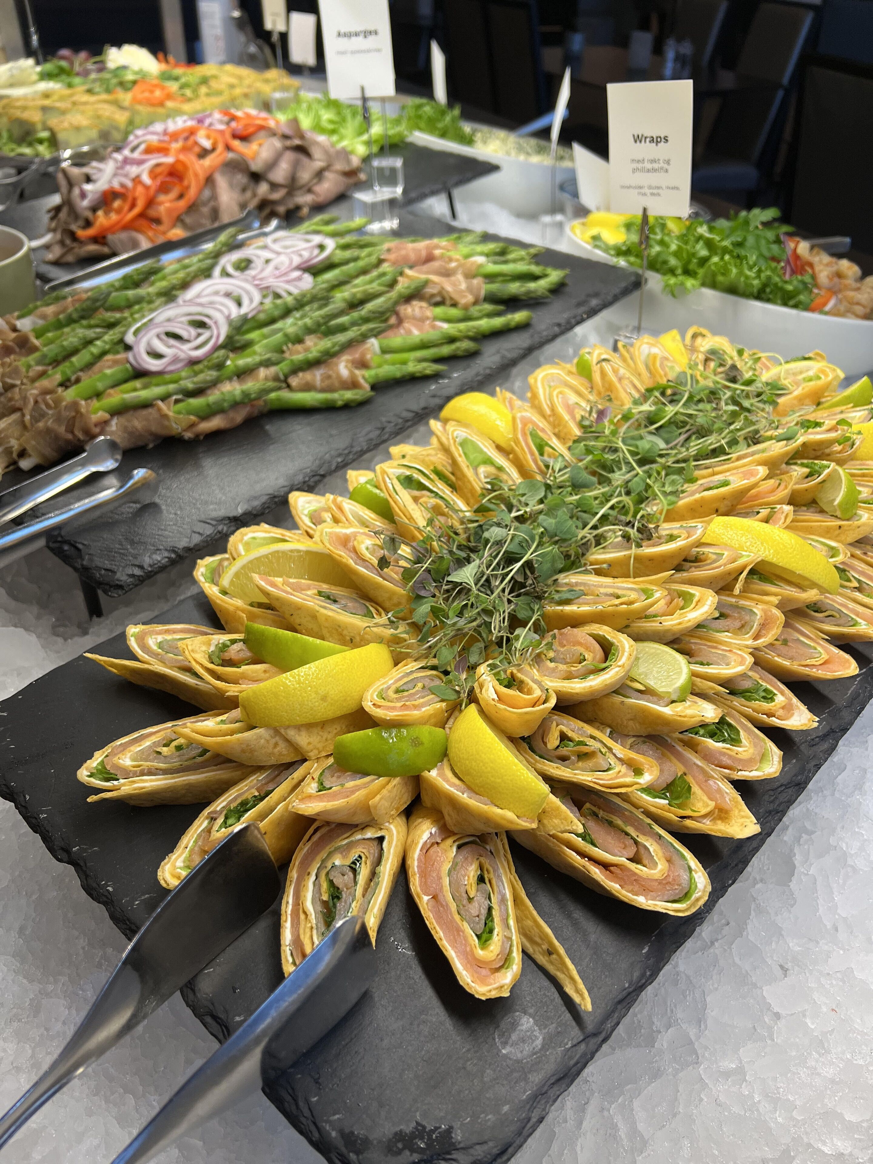 Een buffet met diverse gerechten, waaronder wraps, asperges en ander groenteproduct.