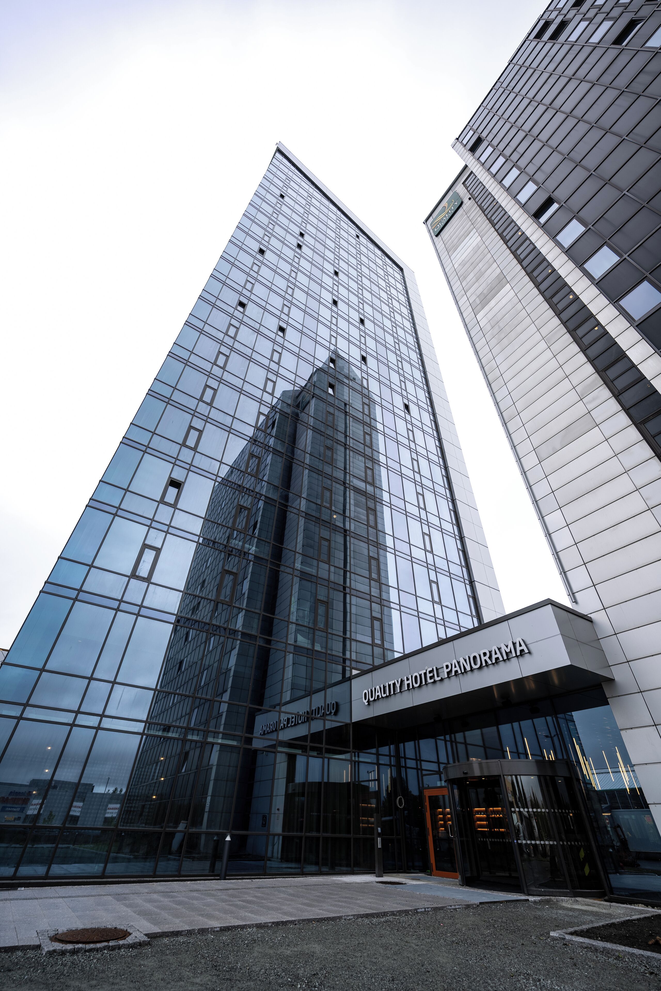 A modern hotel building with a glass facade and a sign reading "Quality Hotel Panorama."
