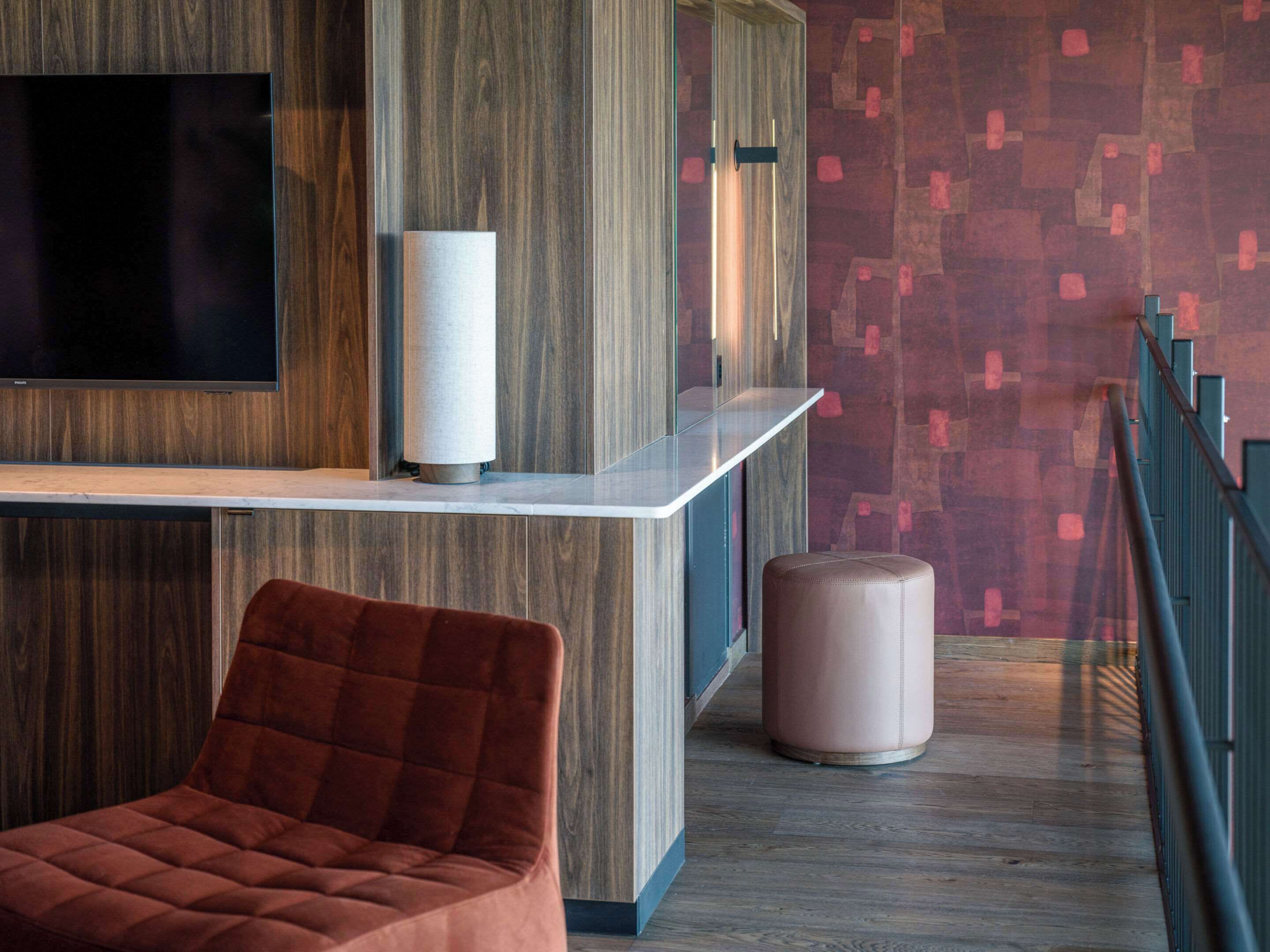 A modern interior with a wooden panel wall, a flat-screen TV, a white console table, a cushioned red chair, and a pink ottoman.