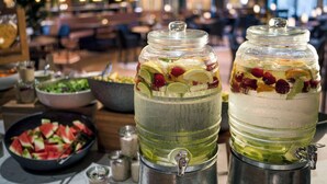 Dos grandes frascos de vidrio llenos de una bebida, sobre una mesa con un bol de ensalada y una bandeja de rebanadas de sandía.