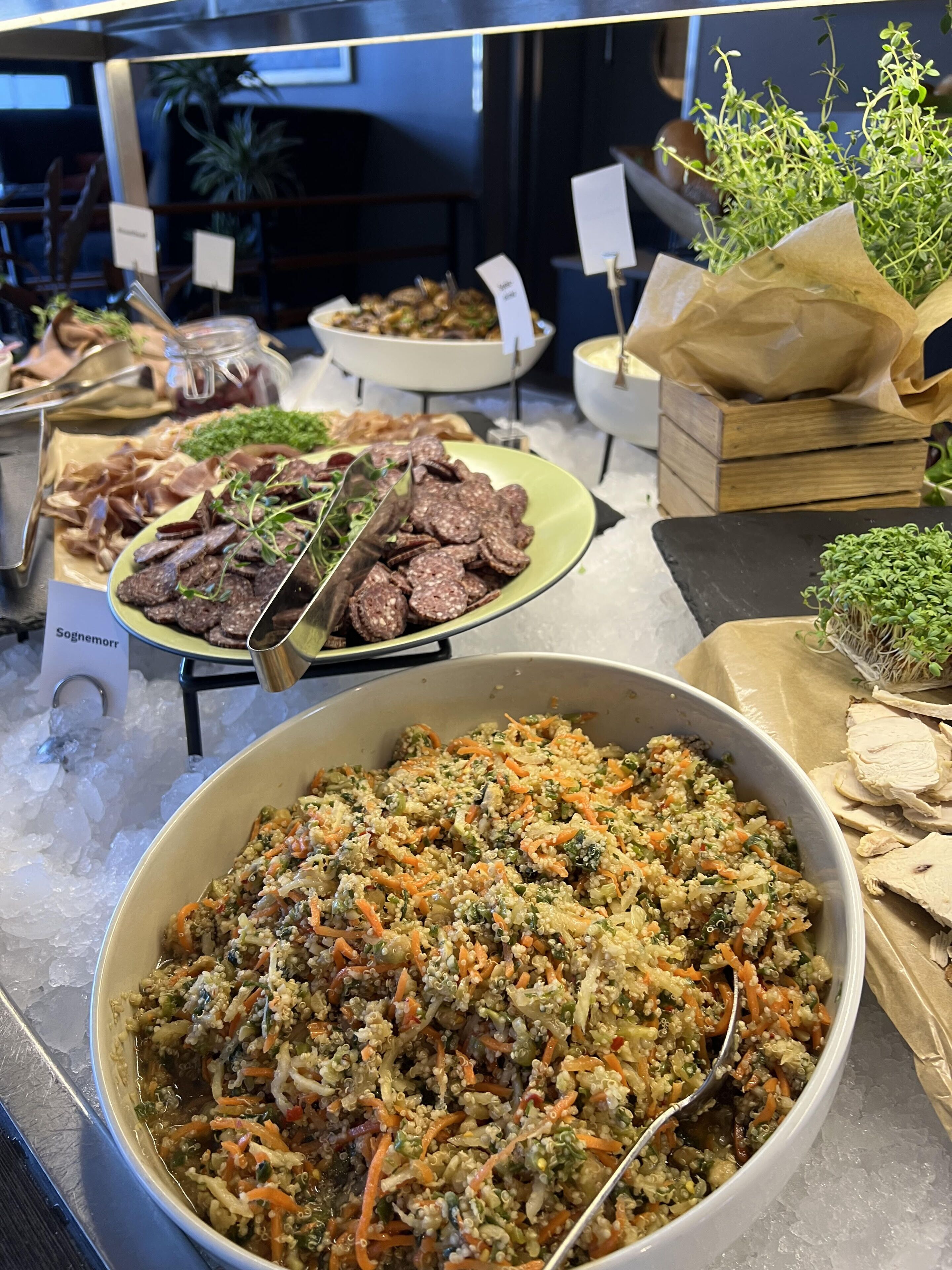Un bufé con diversos platos, incluyendo un tazón grande de ensalada de quinua, carnes en rodajas y hierbas frescas.