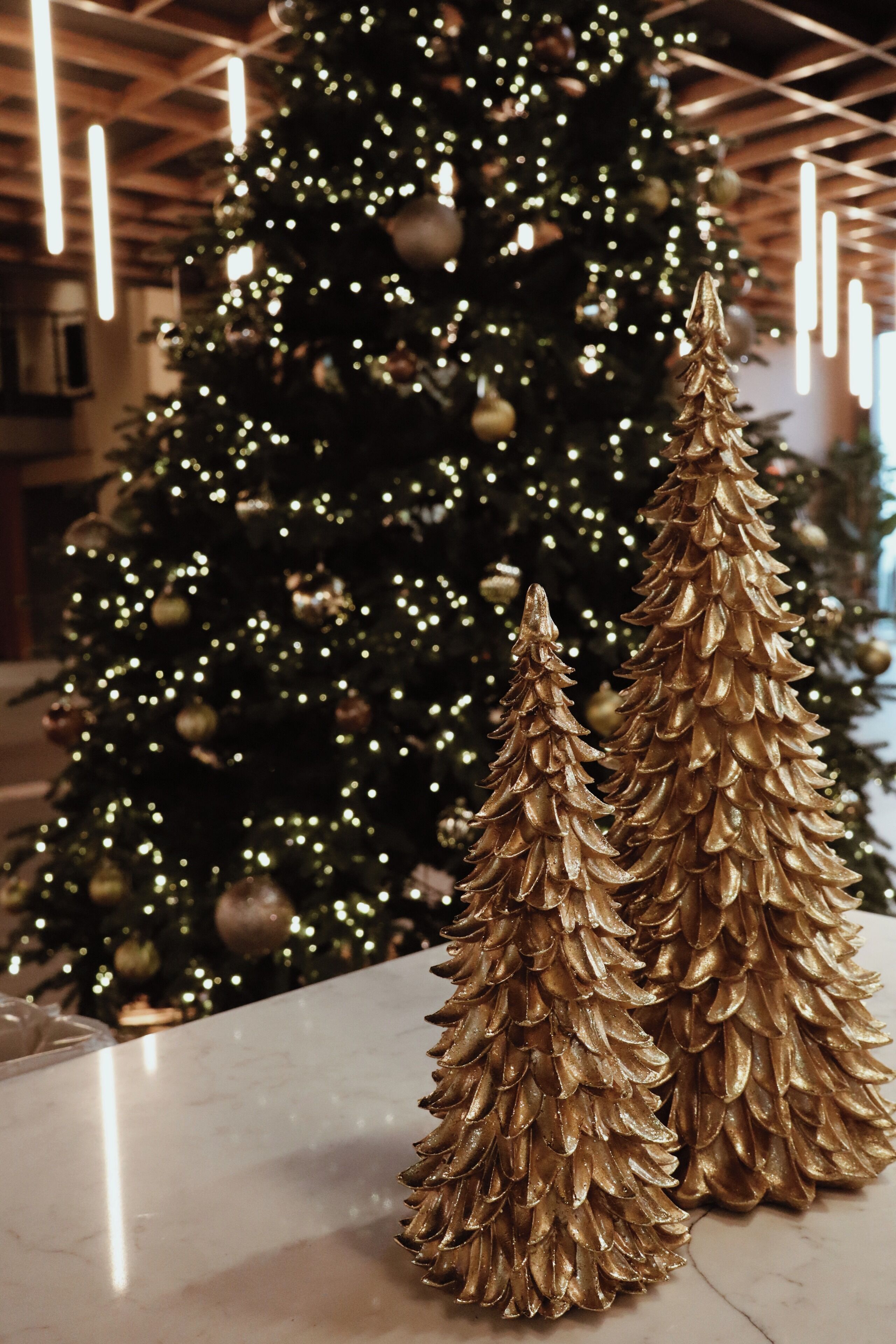 Un árbol de Navidad con luces y adornos, y dos decoraciones de piñas doradas sobre una mesa.