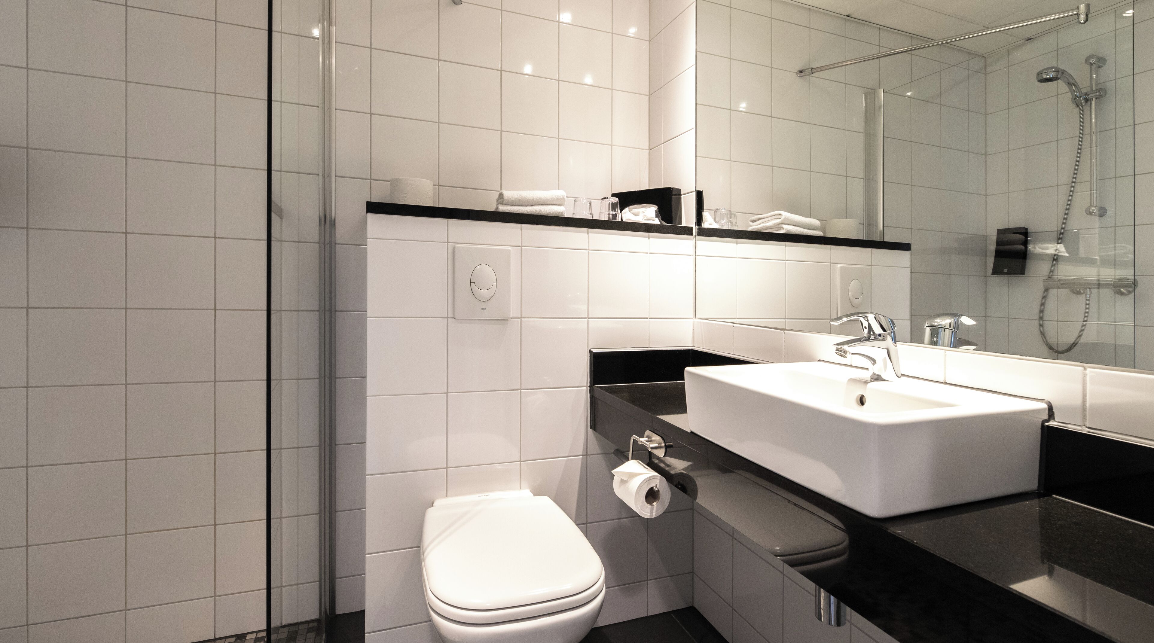 A modern bathroom with a white toilet, a black countertop sink, and a glass shower enclosure.