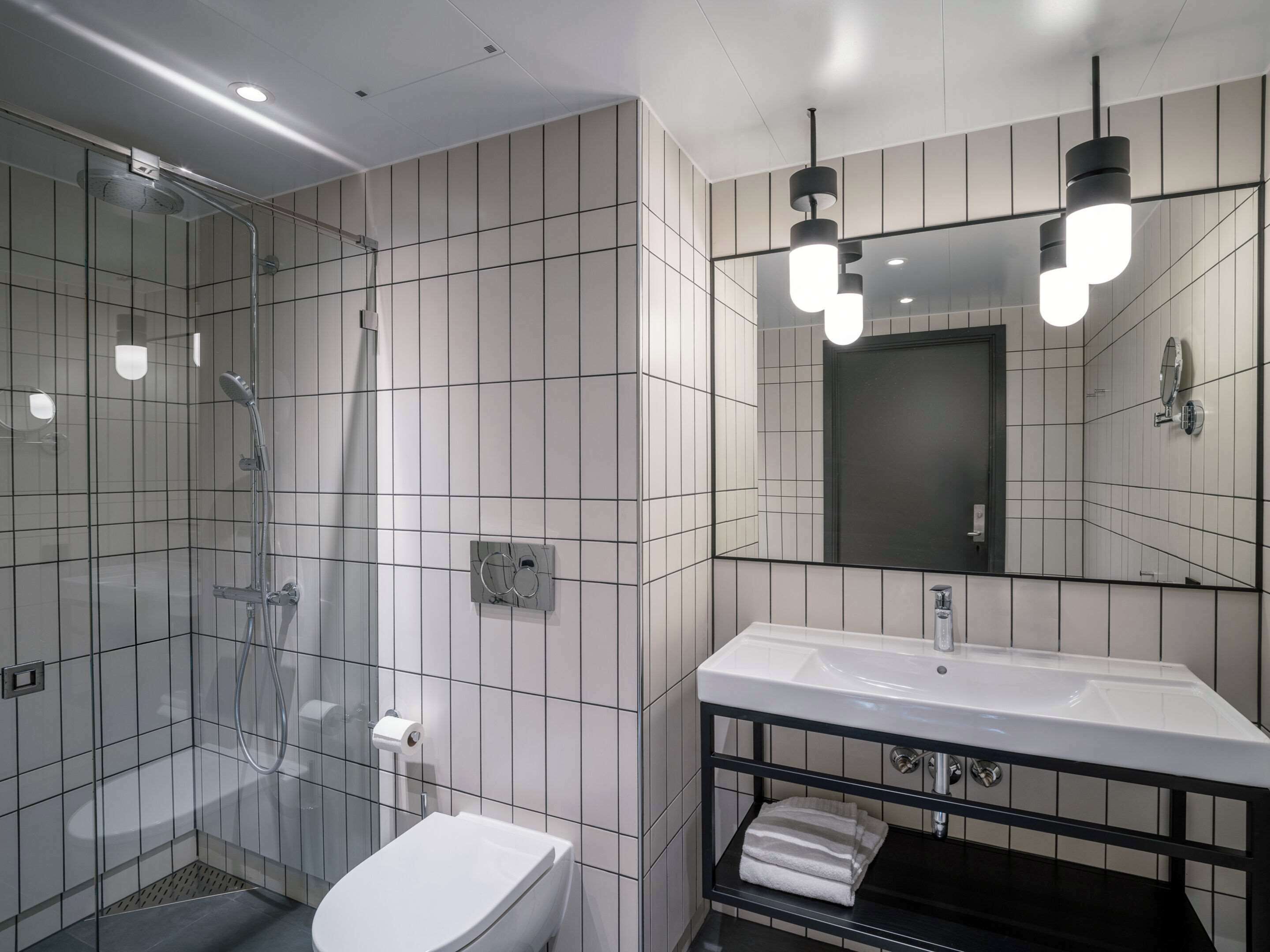 A modern bathroom with a glass shower enclosure, a white toilet, a black vanity with a white sink, and a large mirror.