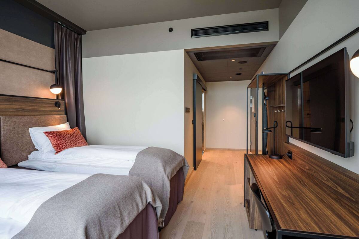 A hotel room with two beds, a desk, a TV, and a mirror.