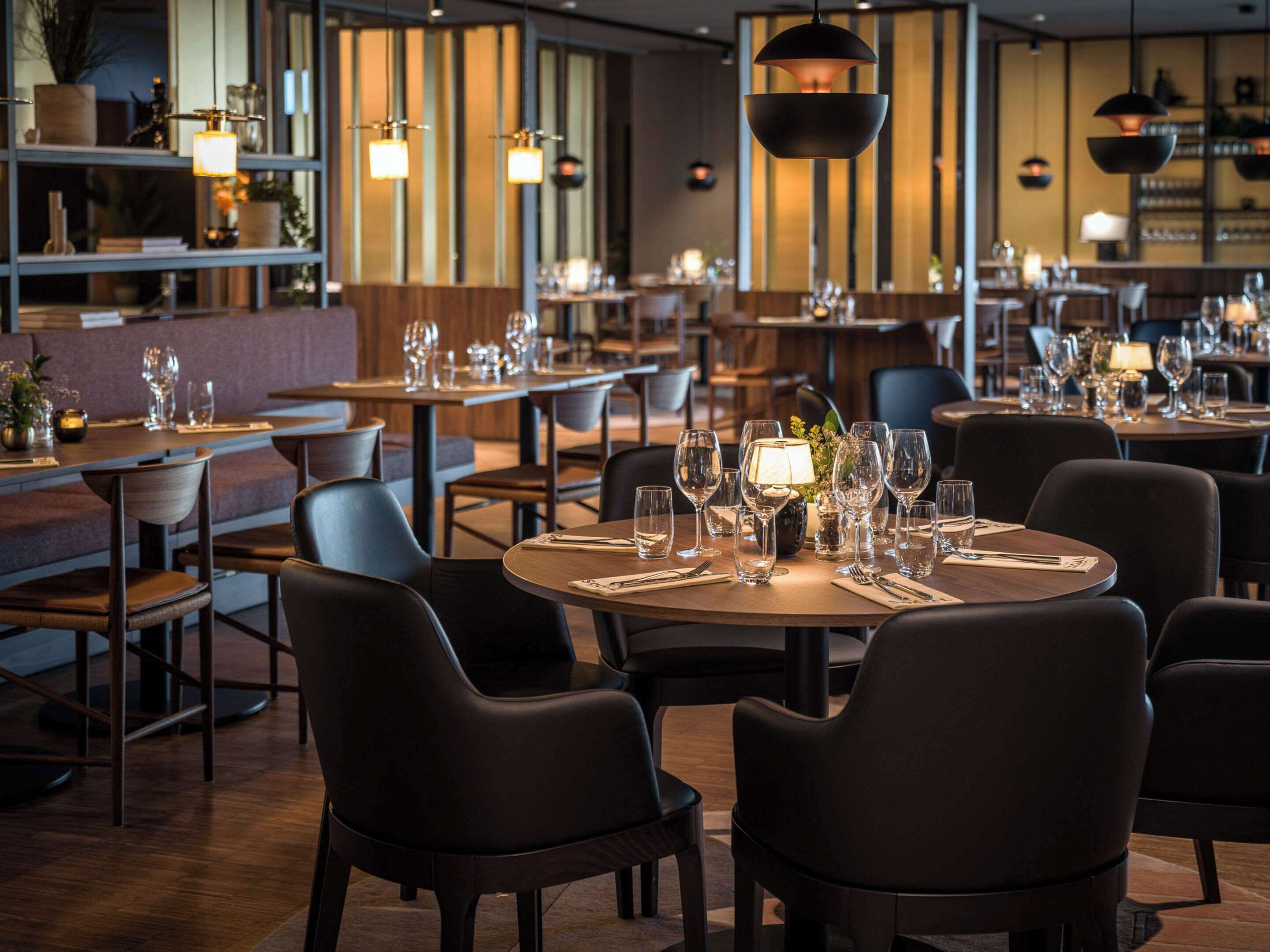 A restaurant interior with round tables, dark chairs, and hanging pendant lights.