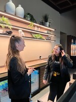 Dos personas conversando en un interior moderno con estanterías de madera, plantas y una pantalla digital.