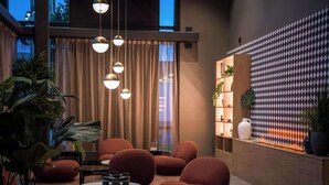Un área de descanso moderna con sillones tapizados en rojo, una mesa de centro redonda de madera y lámparas colgantes.
