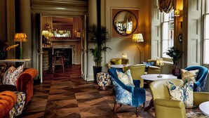 Un hall d’entrée spacieux avec un sol à carreaux, des coins salon confortables et un grand miroir au mur.