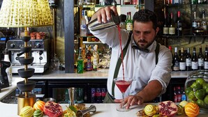 Un barman en train de préparer un cocktail dans un bar, avec des étagères remplies de bouteilles d’alcool en arrière-plan.