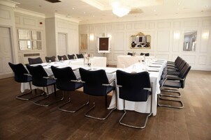 Un salón de conferencias con una larga mesa, sillas negras, manteles blancos y un candelabro.