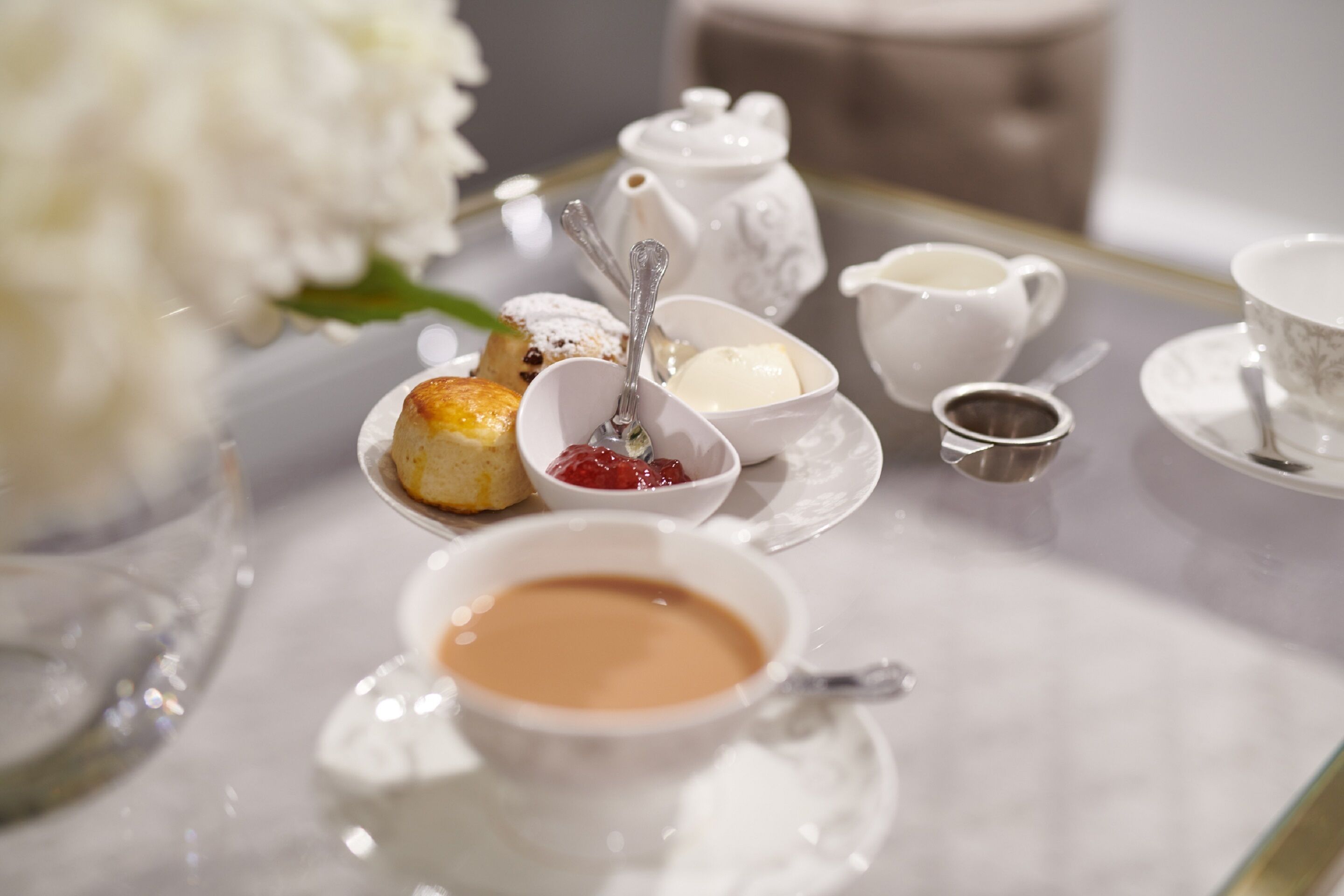 A table set with a teapot, cups, saucers, a teapot, a small bowl with jam, a small bowl with butter, and a small cup of tea.