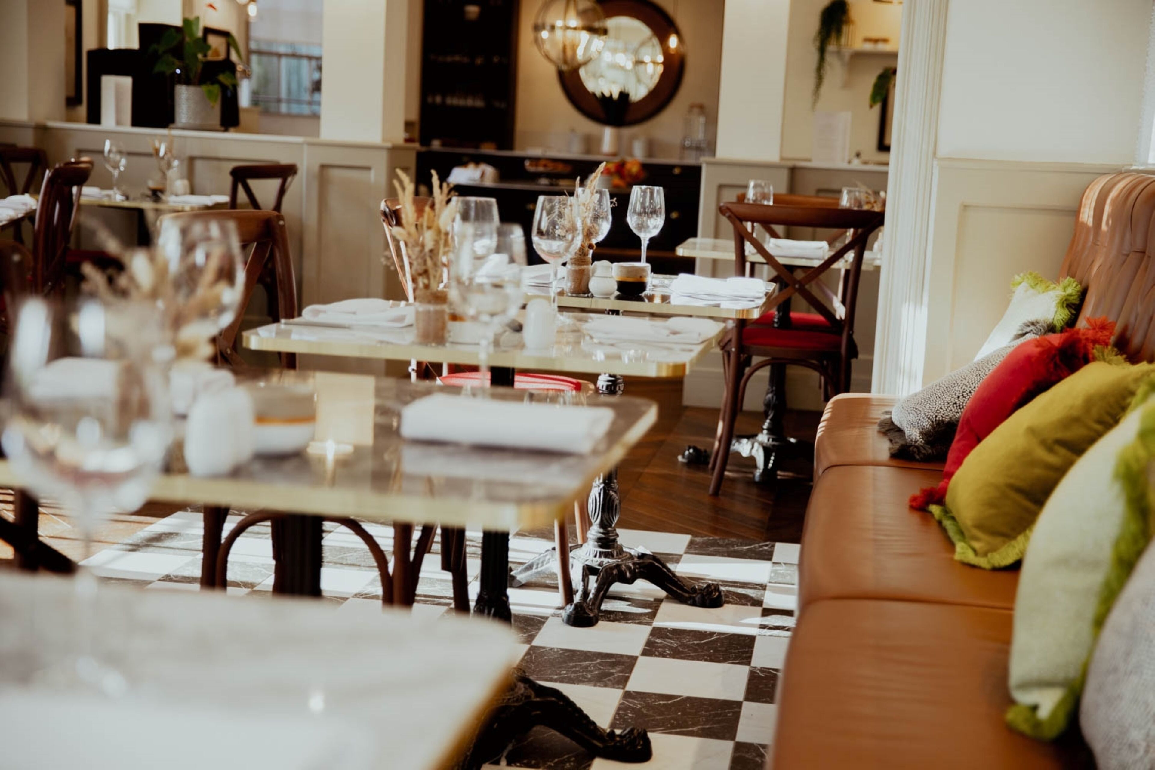 A dining area with tables set for a meal, a checkered floor, and a sofa with colorful cushions.