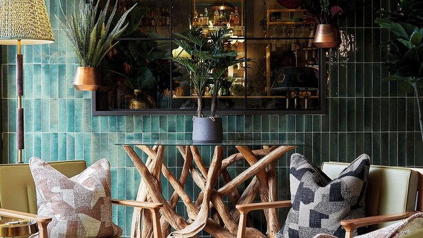 Un coin salon accueillant avec des fauteuils à revêtement vert, des tables basses en bois et des coussins décoratifs.