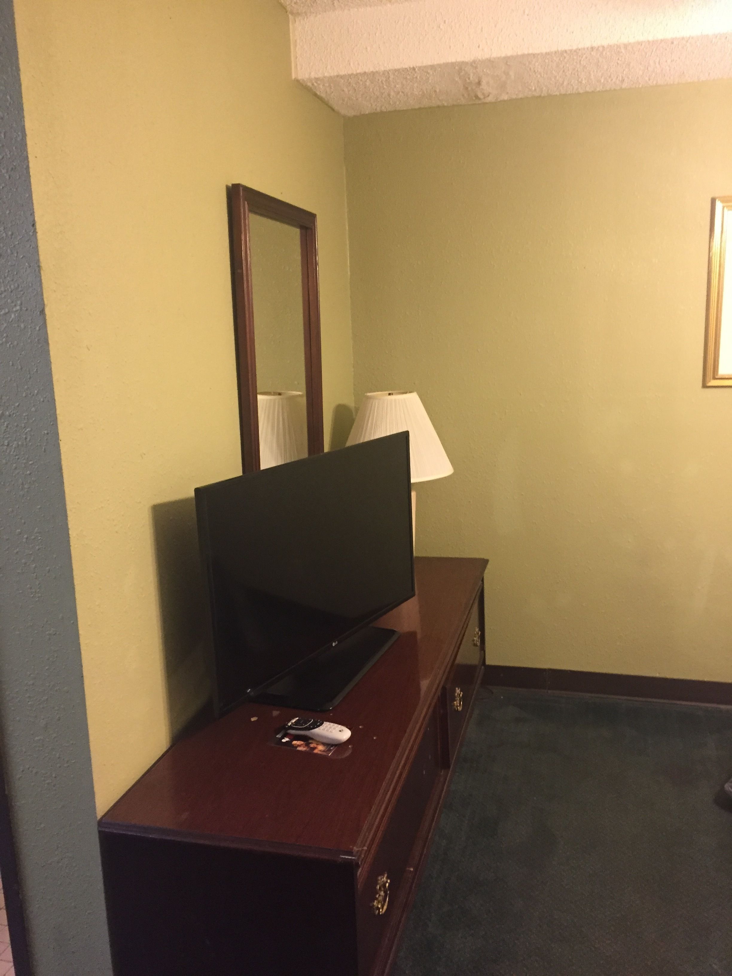 A room with a television on a wooden dresser, a mirror, a lamp, and a carpeted floor.
