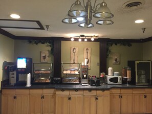 A kitchen with a coffee machine, a microwave, and a display case with pastries. - Rodeway Inn & Suites Smyrna - Nashville Area (Smyrna)