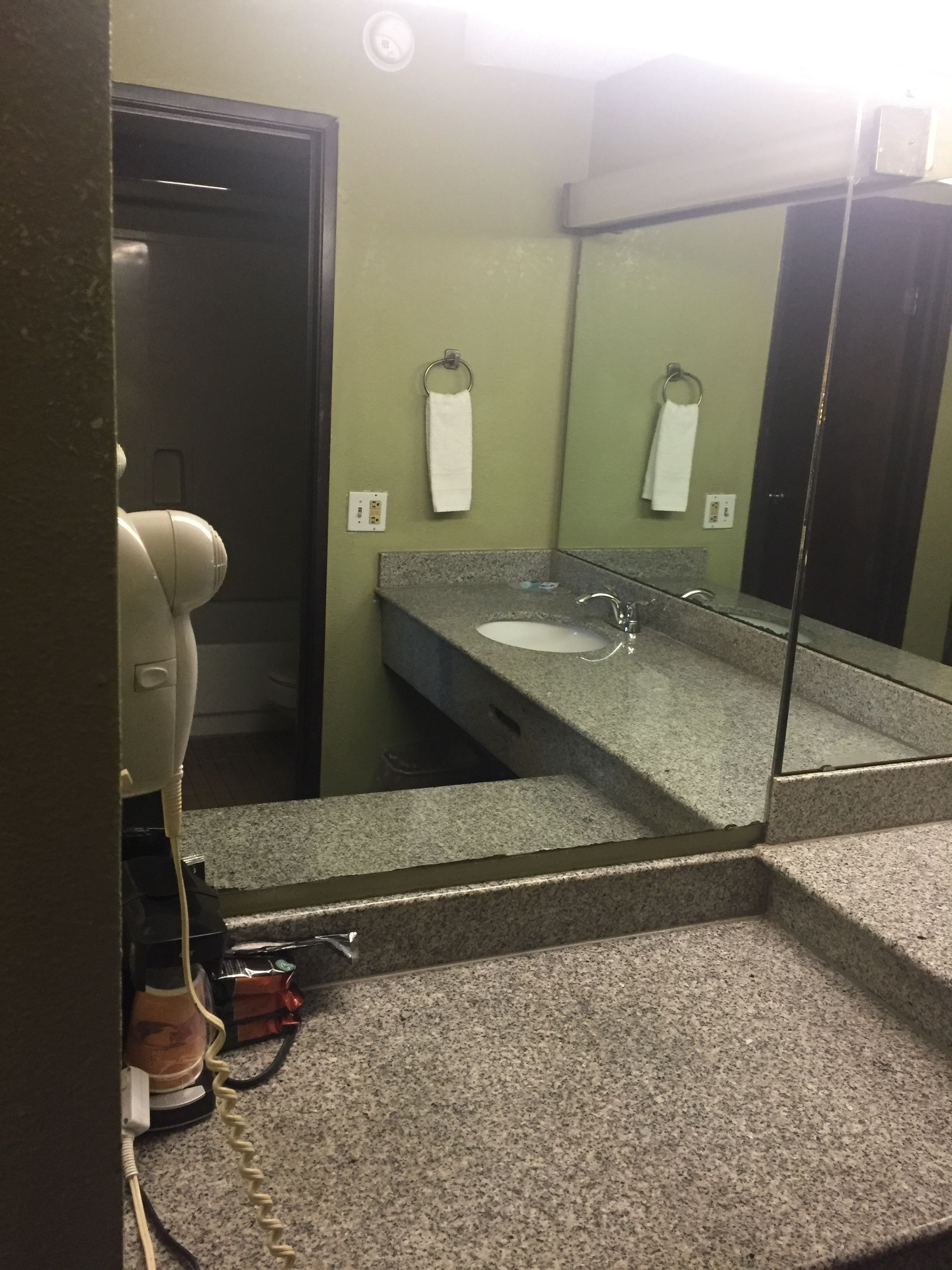 A bathroom with a granite countertop sink, a mirror, and a hairdryer on the floor.