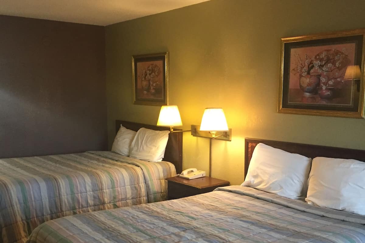 A hotel room with two beds, each with striped bedding, a nightstand with a lamp, and a painting on the wall.