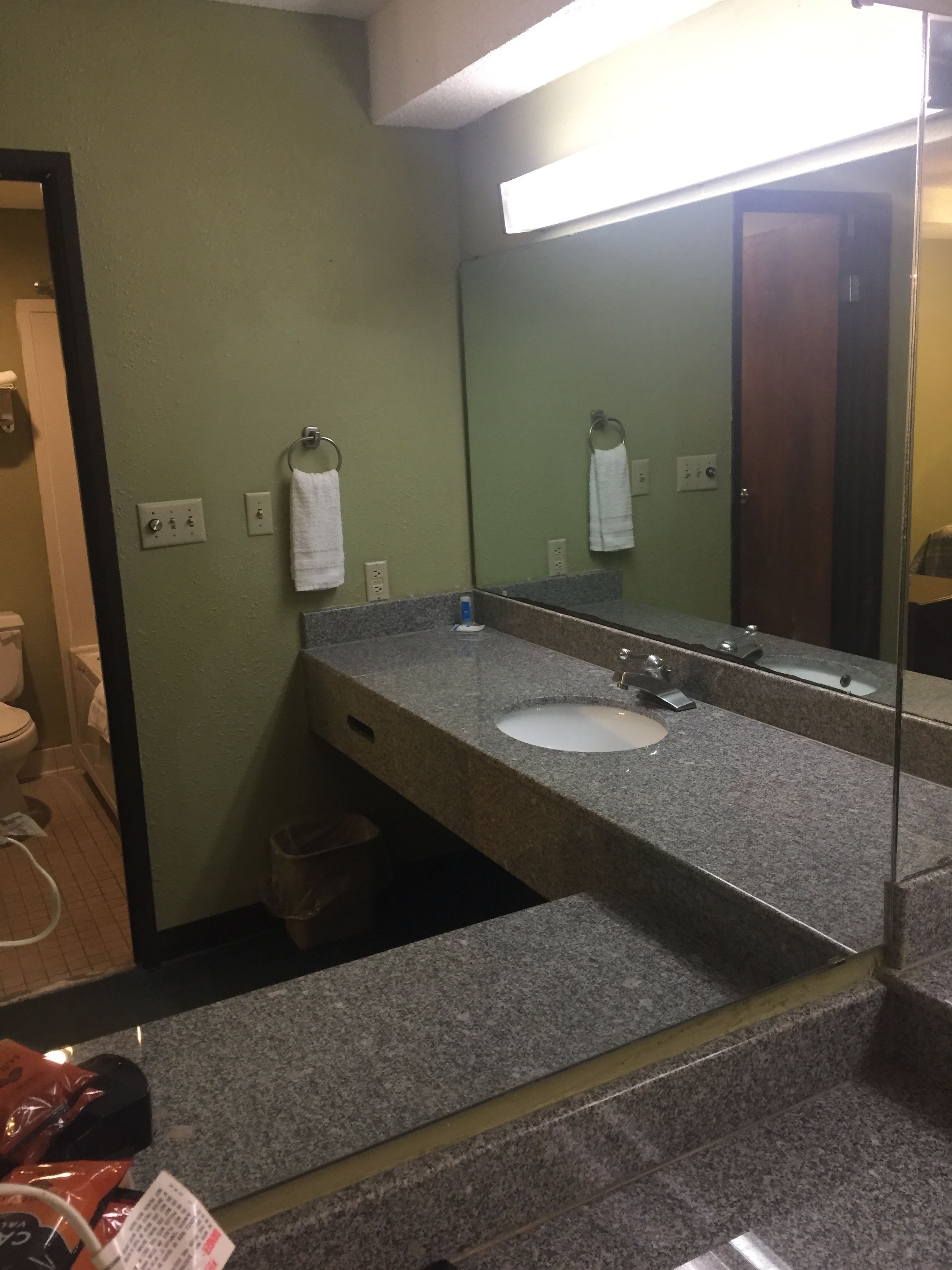 A bathroom with a granite countertop, a white sink, a mirror, and a towel rack.