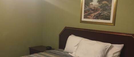 Habitación de hotel con cama, mesita de noche, un cuadro en la pared y una lámpara en el techo.