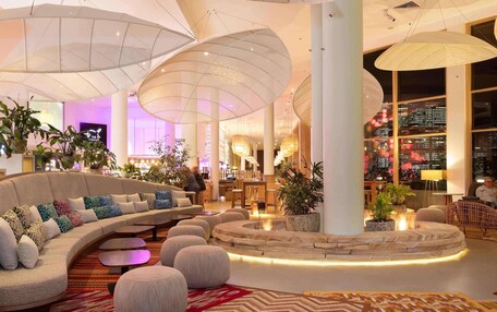 A modern lobby with a curved sofa, round ottomans, and large hanging lamps.