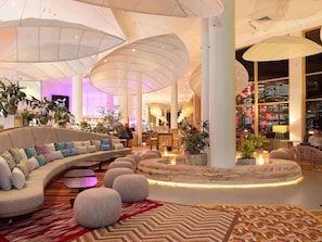 A modern lobby with a curved sofa, round ottomans, and large hanging lamps.