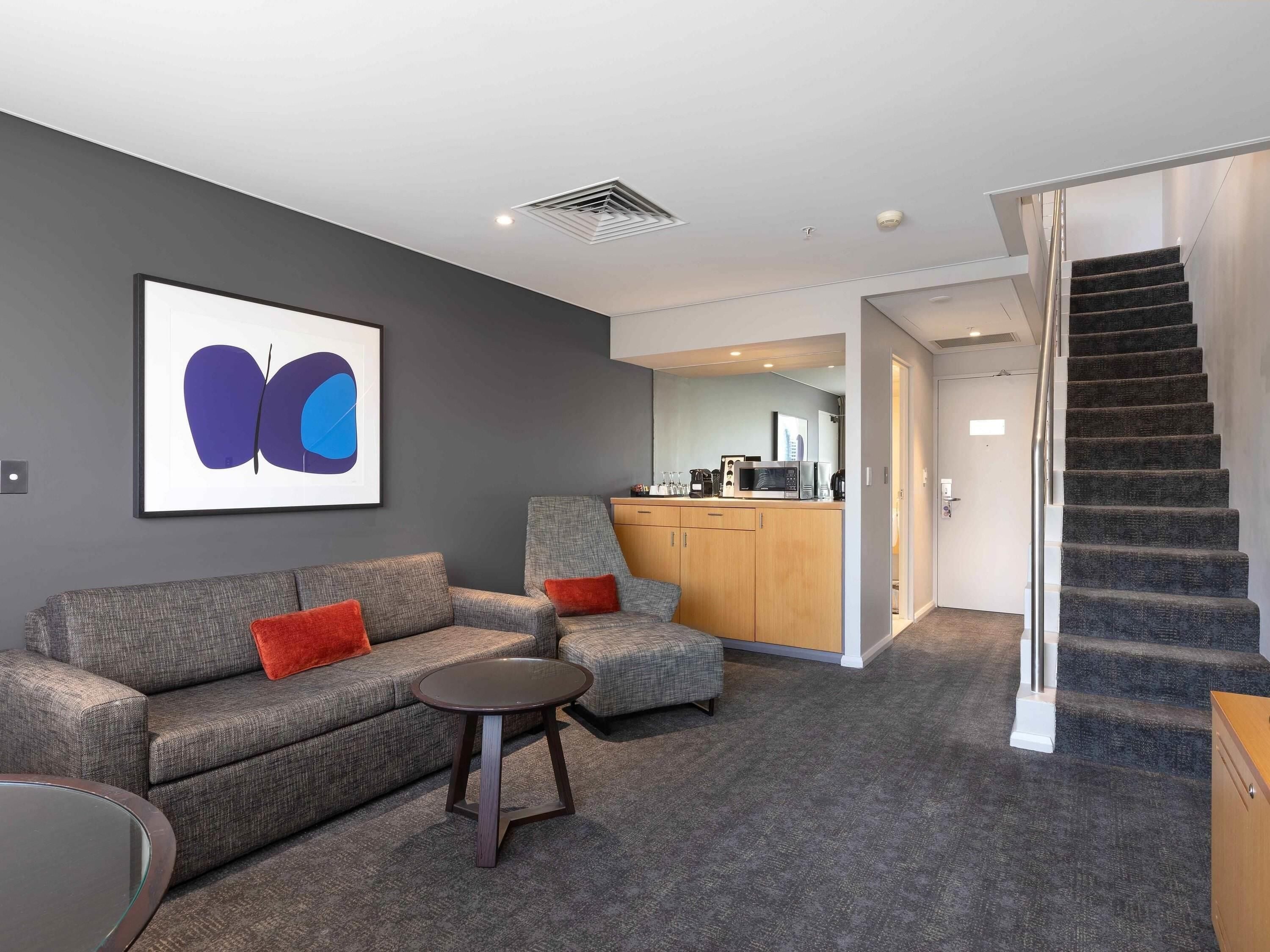 A modern living room with a grey sofa, a small round table, and a staircase leading to an upper floor.