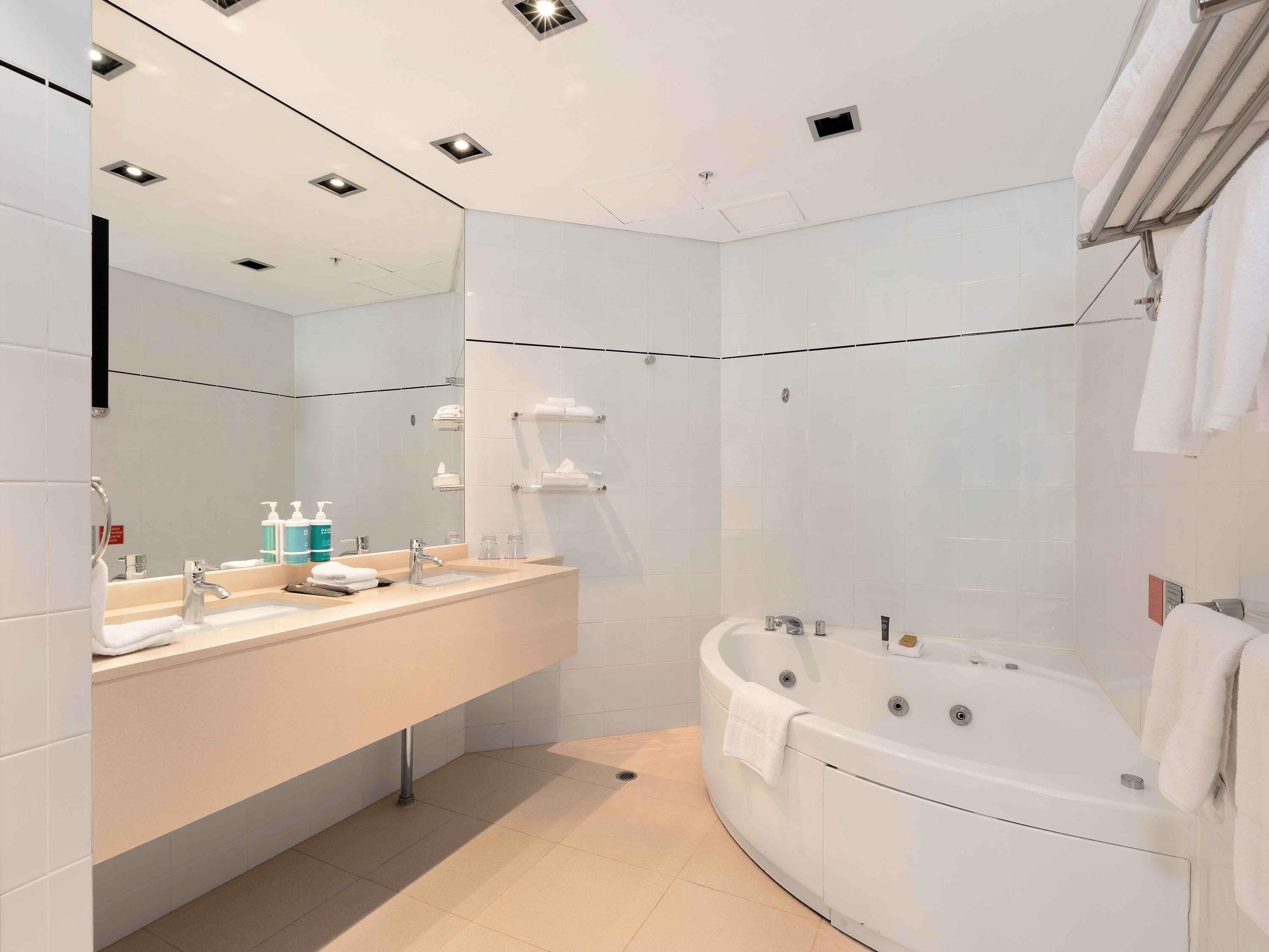A modern bathroom with a large mirror, two sinks, a bathtub, and a shower area.