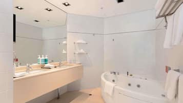 A modern bathroom with a large mirror, two sinks, a bathtub, and a shower area.