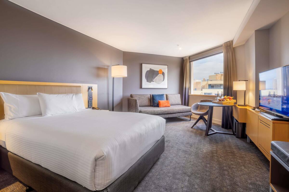 Ett hotellrum med en stor säng, en soffa, ett skrivbord med en dator och en tv.