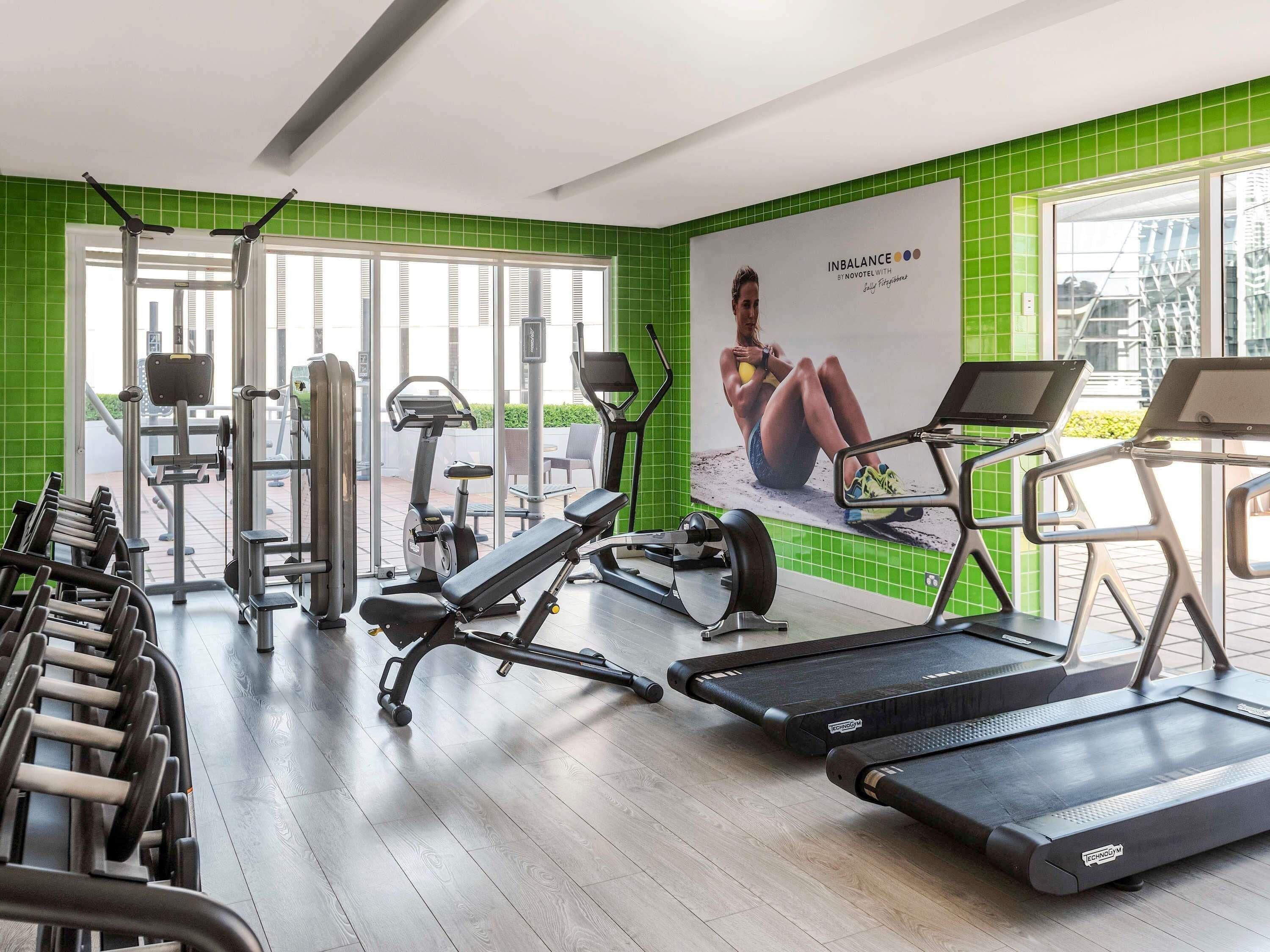 Un gimnasio con cintas de correr, máquinas de pesas y un cartel grande en la pared.
