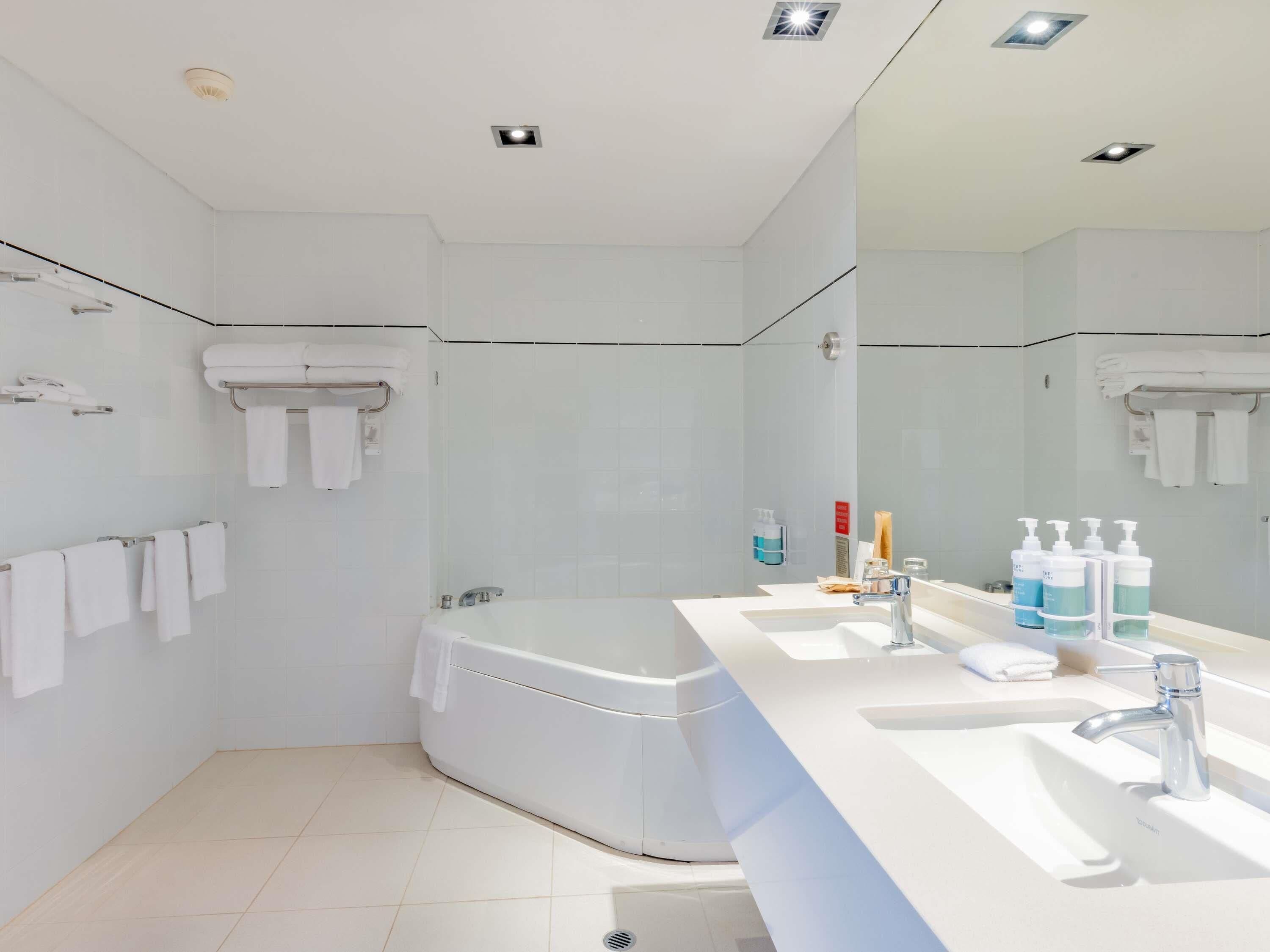A modern bathroom with a bathtub, two sinks, and a large mirror.