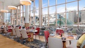Un restaurante moderno con amplios ventanales que ofrecen vistas a la ciudad, suelo de madera y mobiliario contemporáneo.
