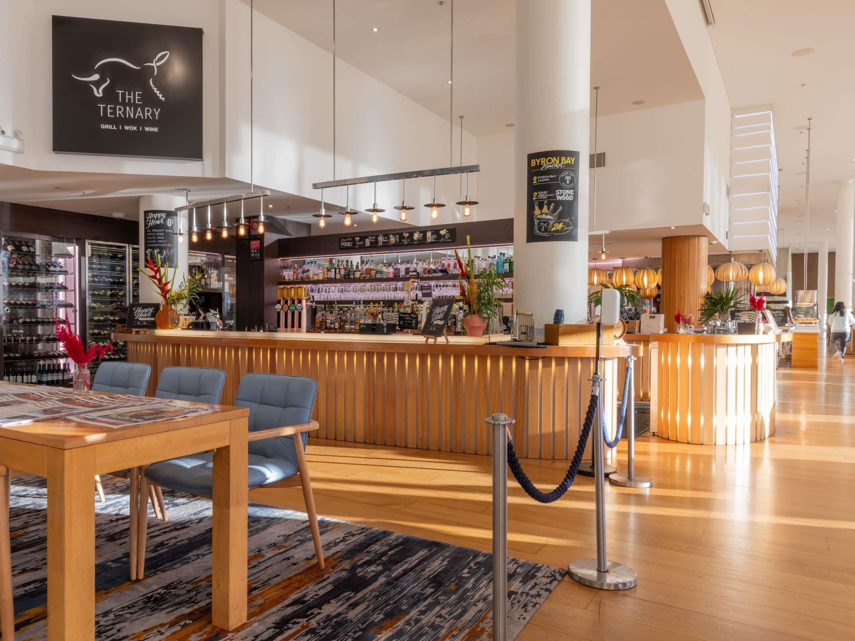 A modern bar area with a wooden counter, bar stools, and a wine rack in the background.