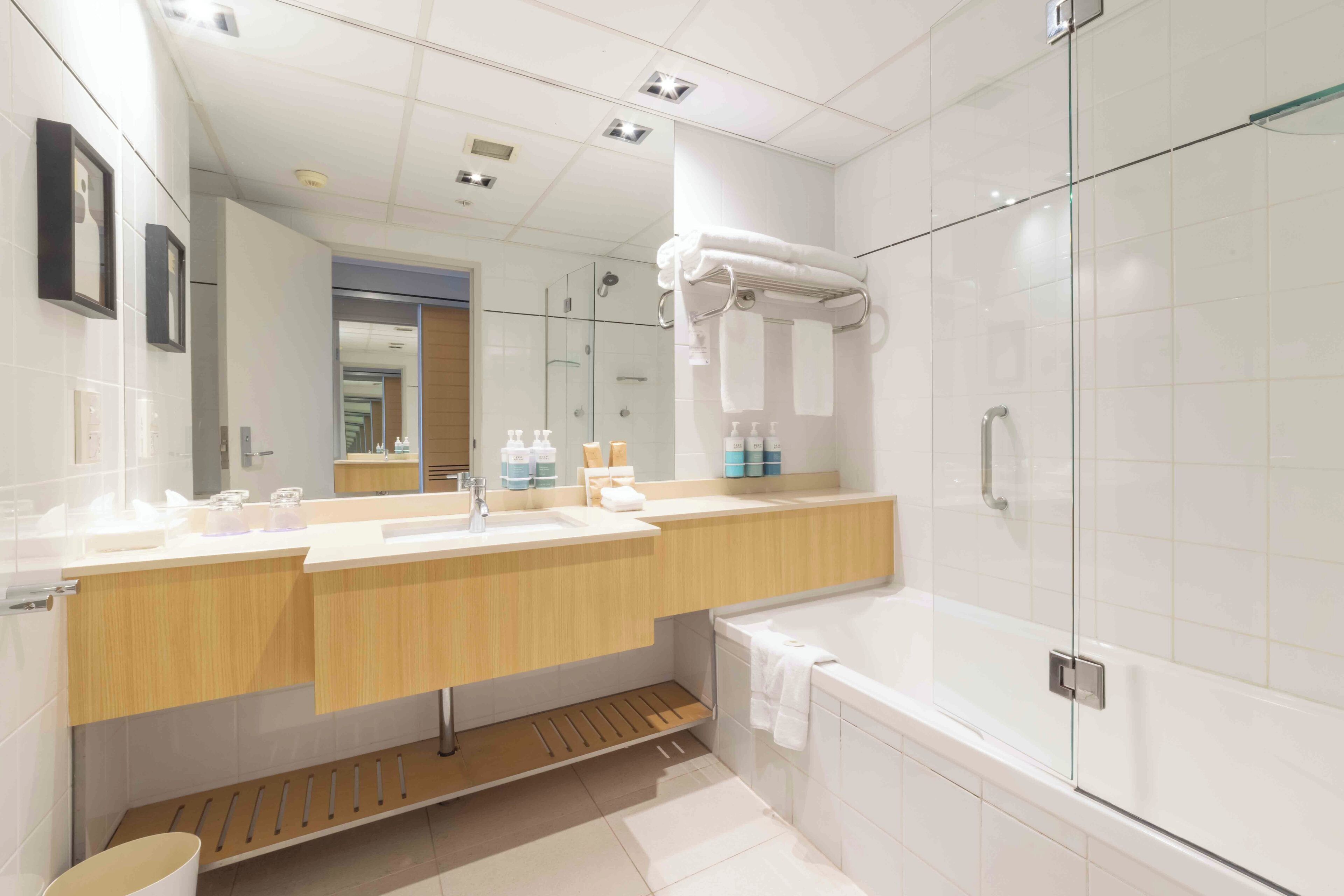 A modern bathroom with a large mirror, a glass-enclosed shower, and a wooden vanity.