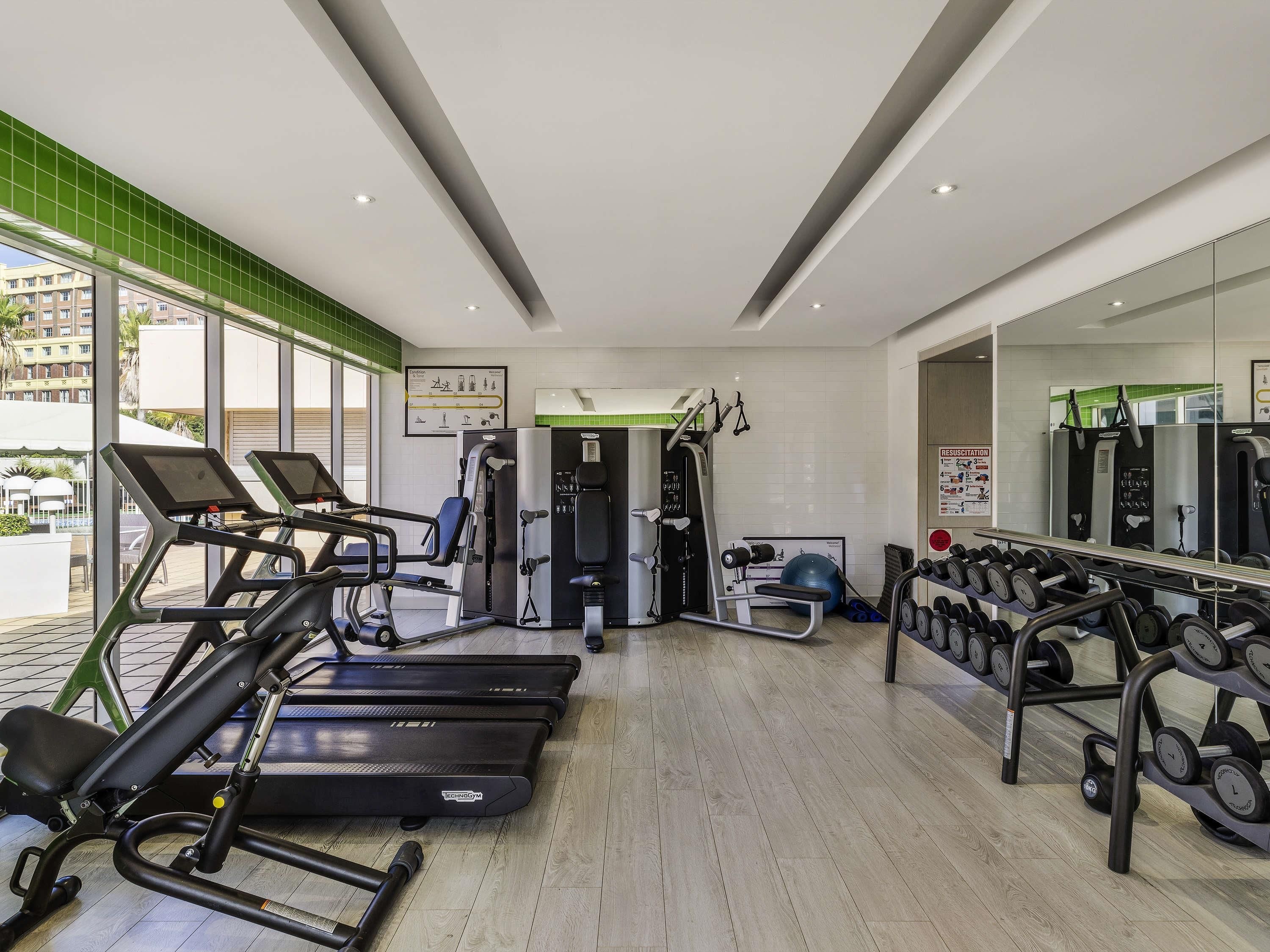 Un gimnasio con cintas de correr, máquinas de pesas y un espejo.