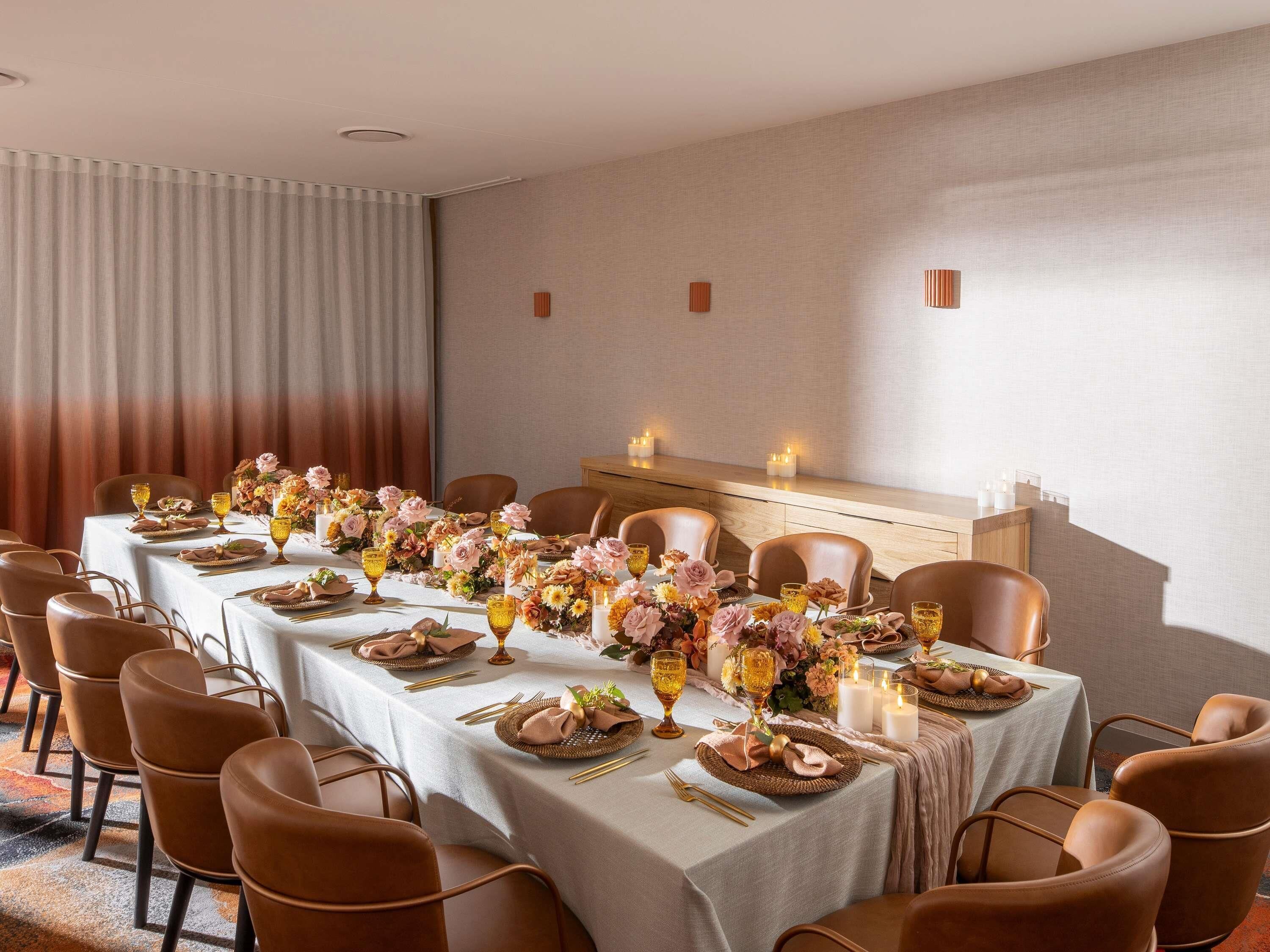 Una larga mesa de comedor con sillas, velas y centros de mesa florales.