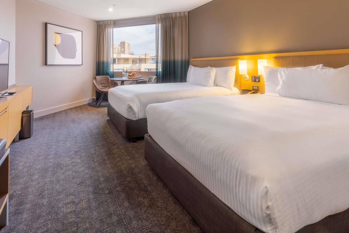 Ett hotellrum med två sängar, ett skrivbord, en stol och utsikt över stadsbilden.