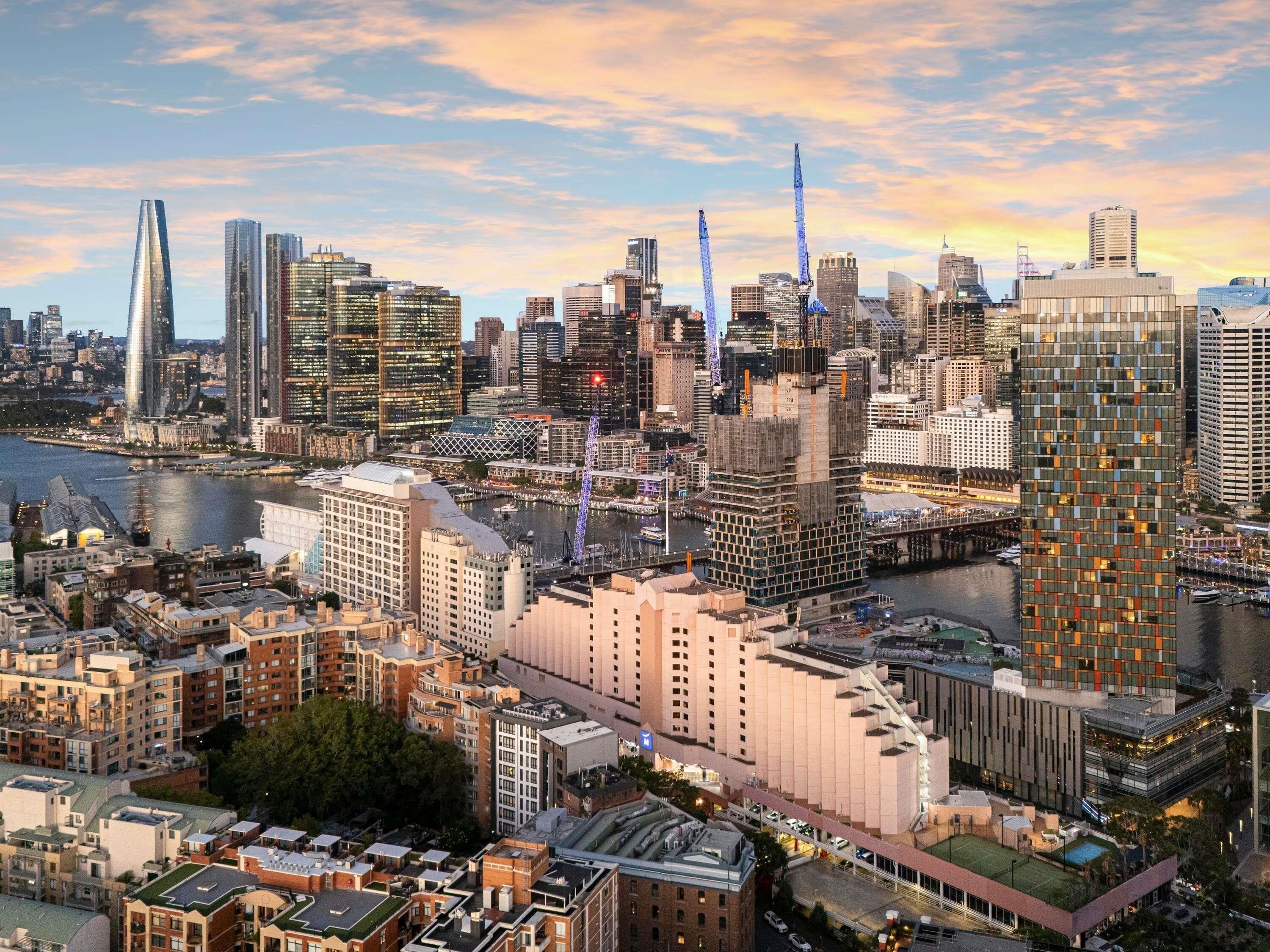 A high-rise hotel with a modern architectural design, located in a bustling cityscape with a river and various other buildings in the background.