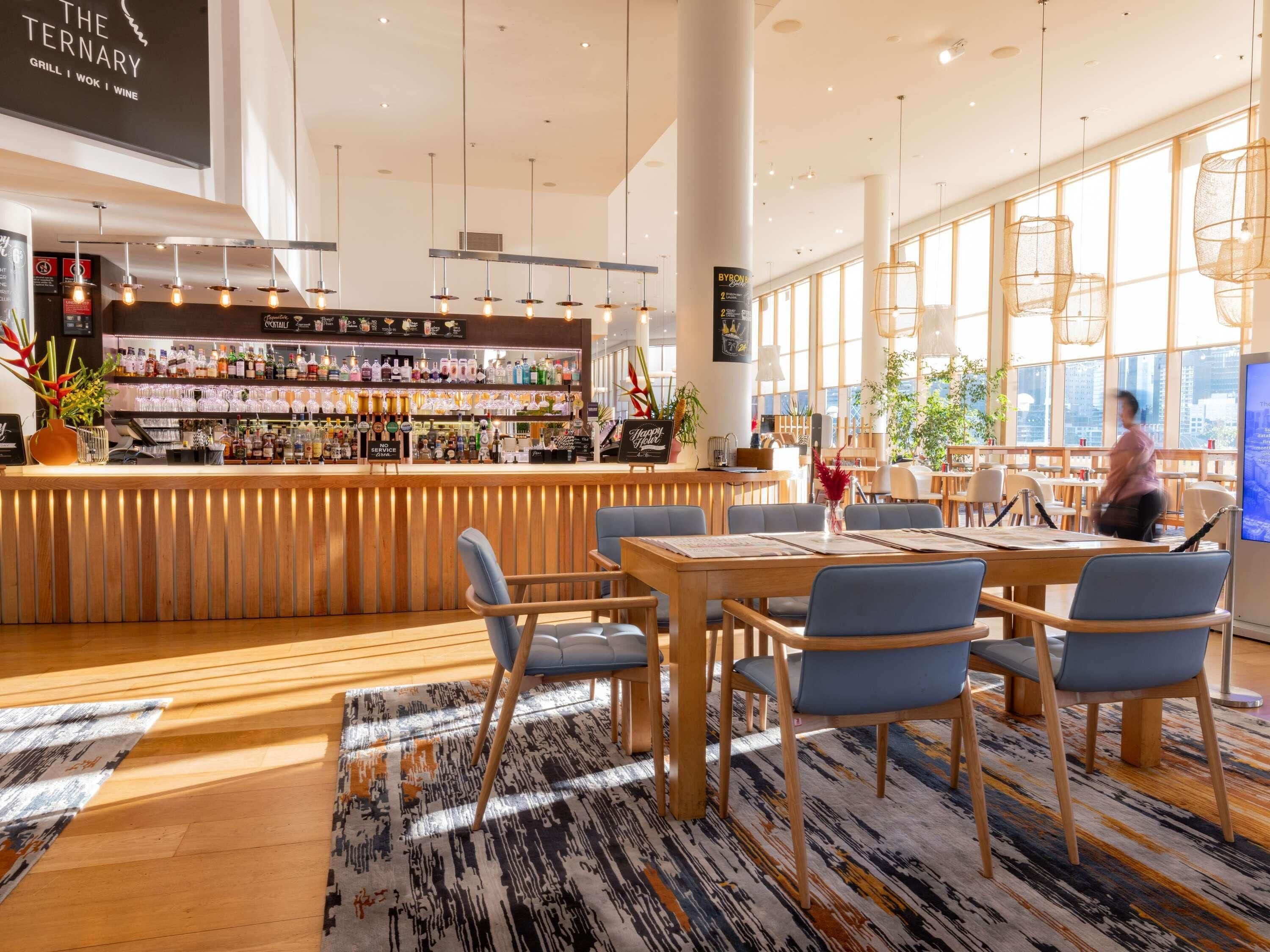 A modern bar area with a wooden counter, bar stools, and a variety of bottles and glasses.