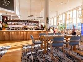 A modern bar area with a wooden counter, bar stools, and a variety of bottles and glasses.