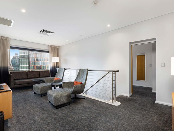 A hotel room with a sofa, two armchairs, a small table, a window with a view of buildings, and a door.