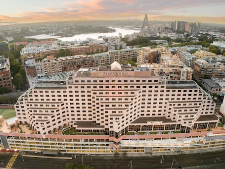 A multi-story hotel with a prominent 'NOVOTEL' sign, a 'THEATERNARY' sign, and a view of the surrounding cityscape and river.