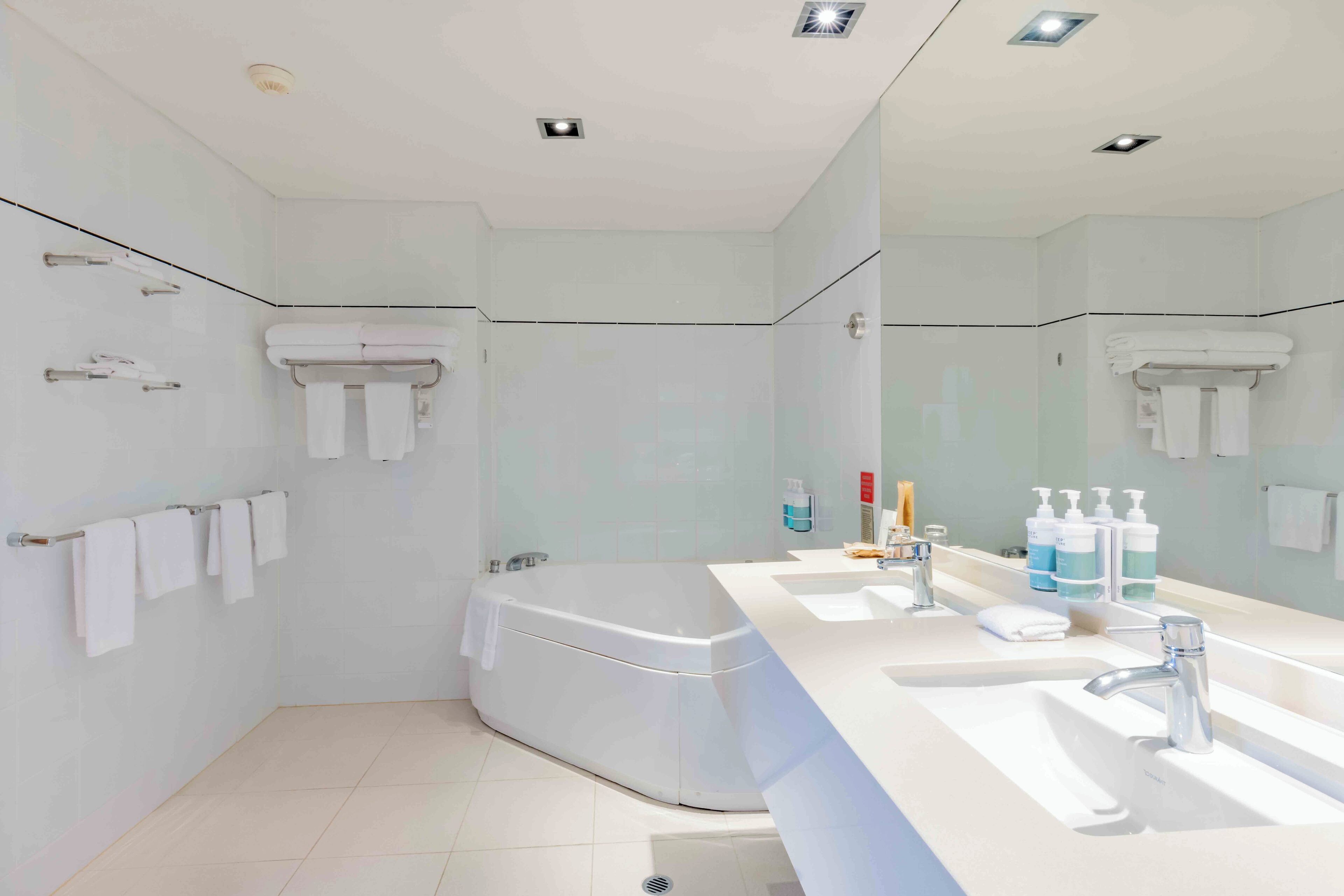 A modern bathroom with a bathtub, a large mirror, and a vanity with toiletries.