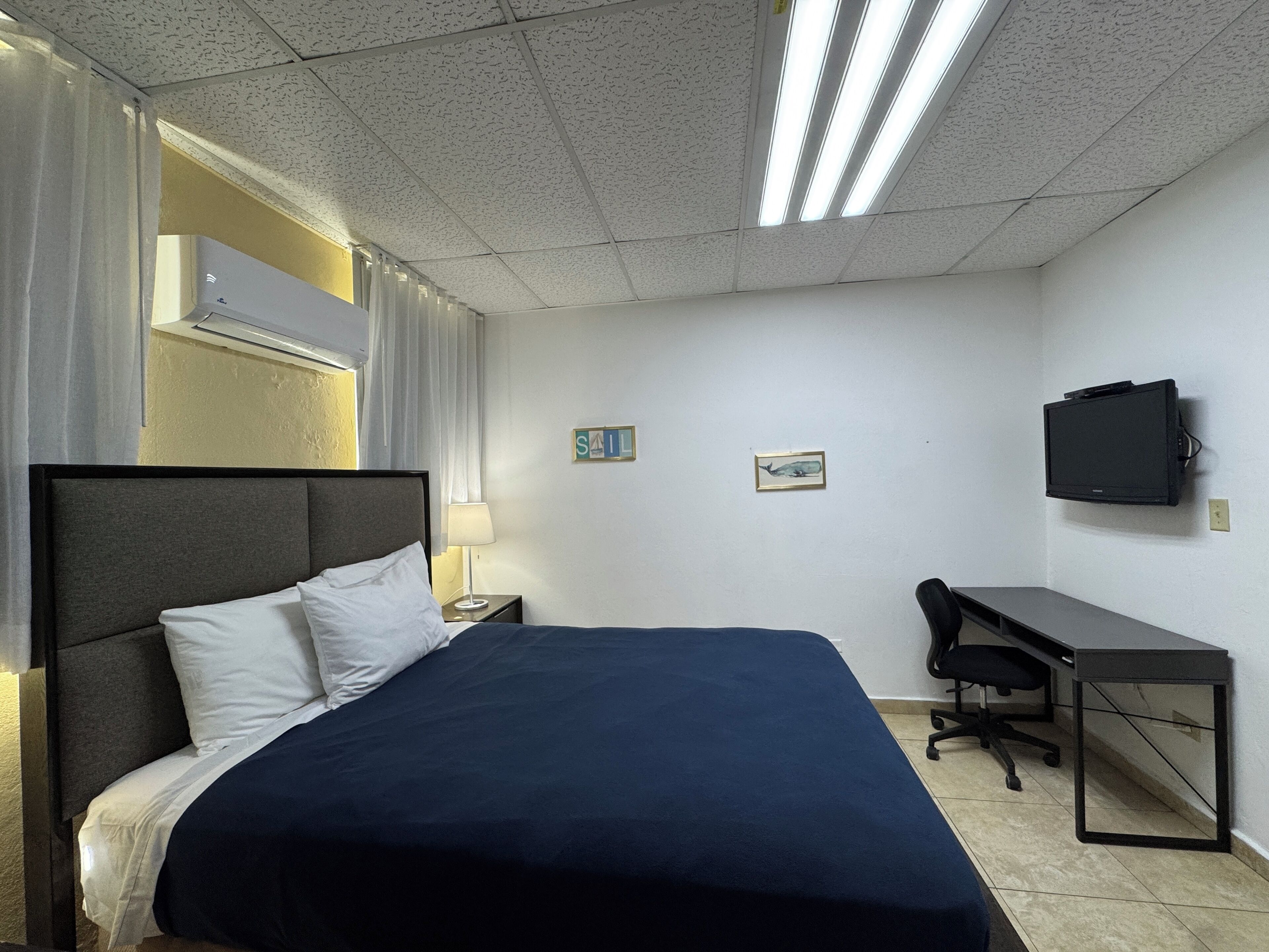 A hotel room with a bed, a desk, a chair, a television, and a window with curtains.