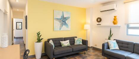 Una sala de estar moderna con un sofá gris, un cuadro grande de estrella de mar, una planta en maceta y una lámpara de pie.