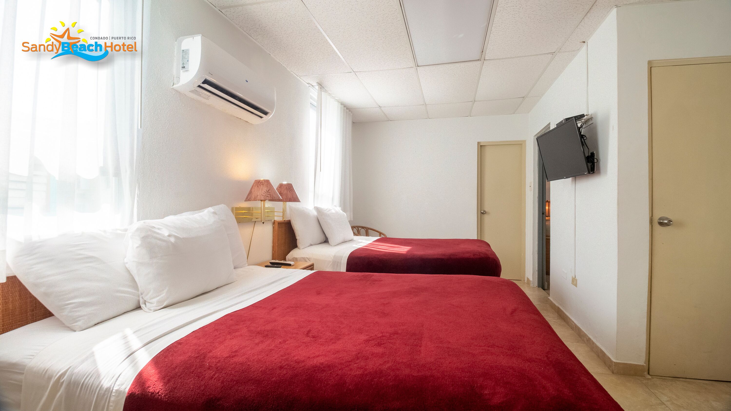 Una habitación de hotel con dos camas, un televisor en la pared y un equipo de aire acondicionado.
