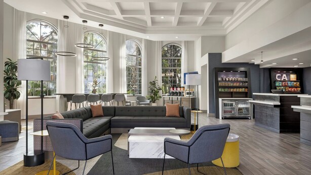 A modern living area with a sectional sofa, two armchairs, a coffee table, and a kitchen area with a refrigerator and shelves. - City Express by Marriott Santa Ana/Orange County Airport (Santa Ana)