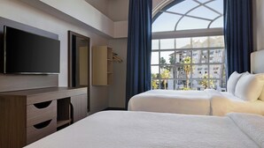 A hotel room with two beds, a TV, a wardrobe, and a large window with a view of buildings. - City Express by Marriott Santa Ana/Orange County Airport (Santa Ana)