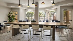 A modern dining area with a long table, white chairs, and hanging pendant lights. - City Express by Marriott Santa Ana/Orange County Airport (Santa Ana)